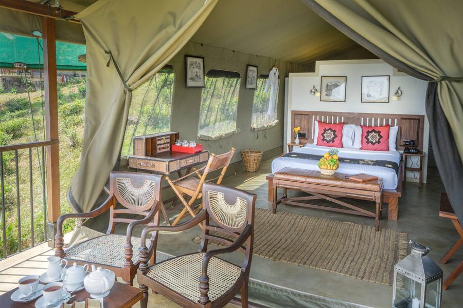 A tented room in tea country with a carved bed, a writing desk and verandah chairs