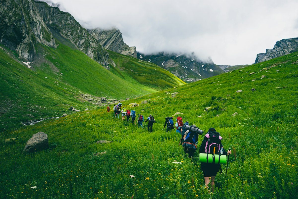 A line of walkers crossing a green valley under the cliffs