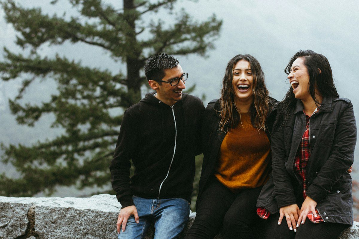 Three friends laughing on a stone wall among pines