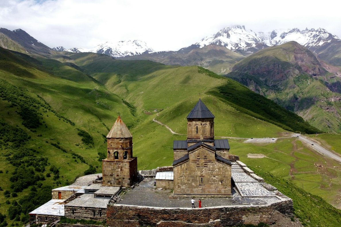 A stone church on a green hill below snow capped peaks in the Caucasus, Georgia