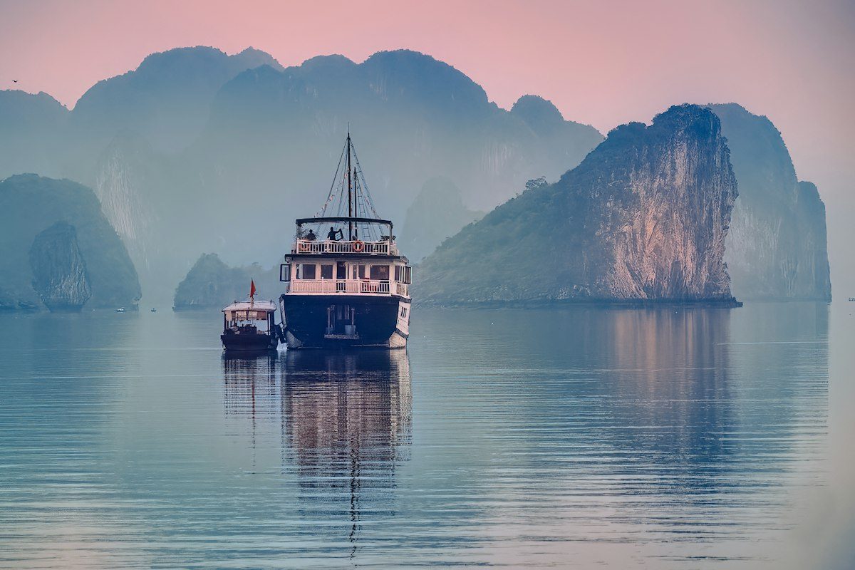 A wooden cruise boat on still water among limestone islands in Vietnam at dusk